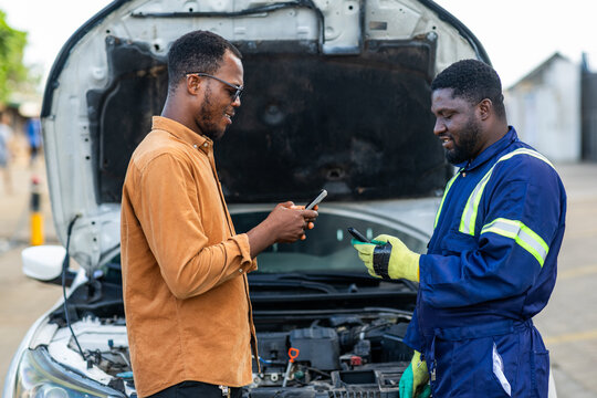 African mechanic receiving mobile money payment from customer after car repair