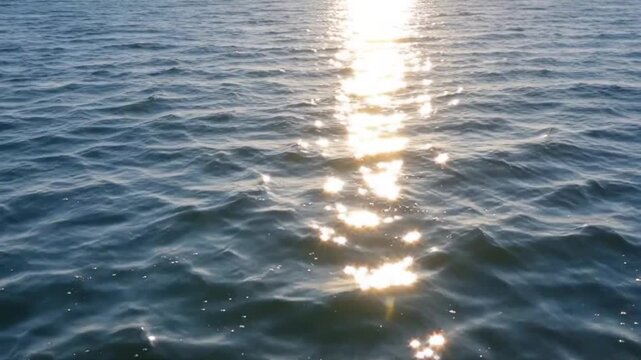 Sun glare sparkling on the water surface. Natural seascape with shimmering reflections of sunlight across gentle waves. Endless ocean view with sun blaze highlighting the texture and movement of the s
