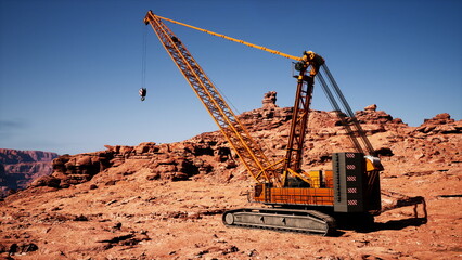 A large crane stands firmly on a rugged landscape, showcasing its powerful design against a stunning backdrop of red rock formations and a bright blue sky.