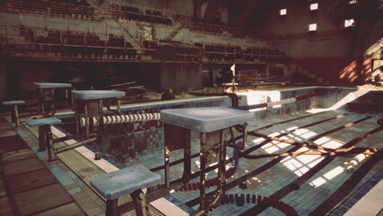 Water laps gently at the abandoned swimming pool as sunlight filters through broken windows. The empty stands hint at past events, while dust covers the once busy lanes of water.