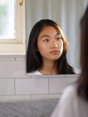Young Asian Woman Looking in Mirror in Bathroom