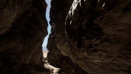 Naklejka premium Sunlight shines through a narrow canyon, with towering rock formations on either side. Sandy ground leads deeper into the beautiful desert scenery, inviting adventure.