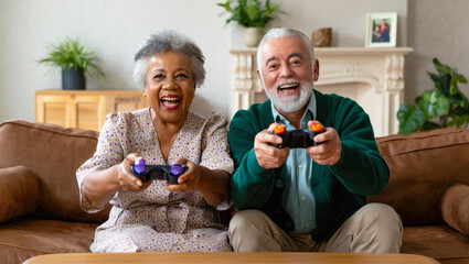happy elderly couple having fun playing video games on couch in living room. happy grandparents playing on console in front of TV. senior with tech, active aging, grandparents with technology