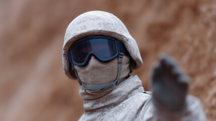 Soldier in camouflage uniform and tactical gear using hand signal for communication during military operation, focused and alert in desert environment