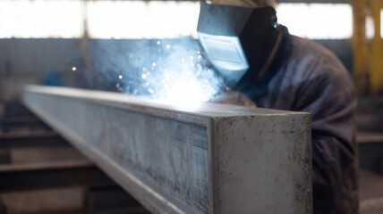 Worker welding metal beam in industrial factory bright sparks and smoke protective helmet heavy industry construction site focused atmosphere skilled labor steel fabrication