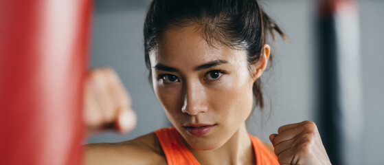 Confident Asian female athlete in orange sportswear practicing boxing in gym, focused expression, close up portrait, fitness training, determination, strength, motivation