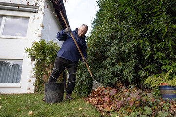 A man removes fallen leaves in an autumn garden.