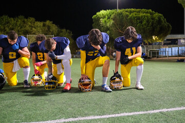 American football players kneeling on a stadium field before a night game