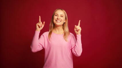 Happy middle aged woman pointing finger up, looking at camera, posing isolated on red background
