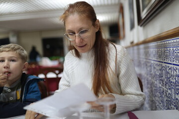 Woman reading menu with boy eating in restaurant