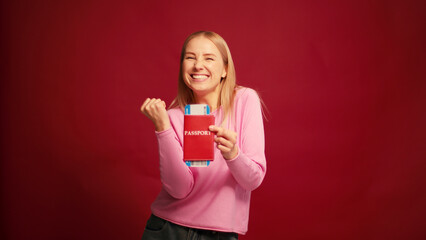 Happy middle aged woman showing passport with boarding pass pointing finger on red background