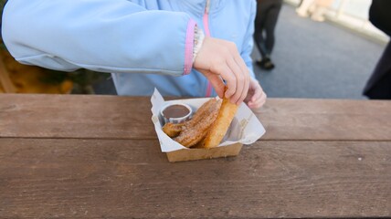 Close-up of a person holding a freshly made churro, dipping it into a small cup of rich chocolate...