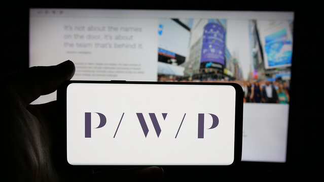 Stuttgart, Germany - 11-19-2025: Person holding cellphone with logo of US company Perella Weinberg Partners (PWP) on screen in front of webpage. Focus on phone display.