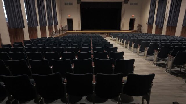 The high school theater awaits its next event, showcasing a large empty stage and clean seating ready for an audience.