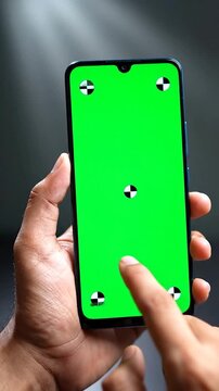 A hand holds a smartphone with a green screen and touches it. Background is dark and simple