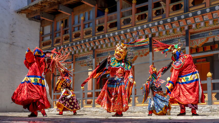 View of vibrant dancers in ornate masks and flowing robes perform a traditional dance against the backdrop of a decorated building, Bumthang, Bumthang, Bhutan.