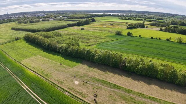 Wide aerial drone shot of Danish countryside farmland, featuring alternating green and brown fields separated by hedgerows and tree lines.