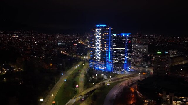 A stunning night aerial view of Sofia showcasing the glowing cityscape and a brightly illuminated Grand Hotel Millennium Sofia rising above the capital.