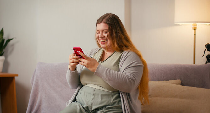 Plus size woman scrolls smartphone while sitting on couch