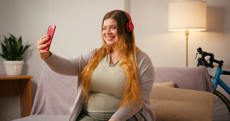 Plus size woman waves at camera talking on smartphone smiling