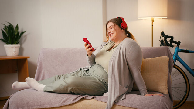 Body positive woman sits on sofa smiling with smartphone in hand - Powered by Adobe