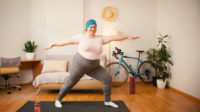Overweight woman does warrior pose on yoga mat for weight loss - Powered by Adobe