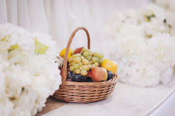 Colorful fruit basket surrounded by white flowers at an elegant event in a bright setting