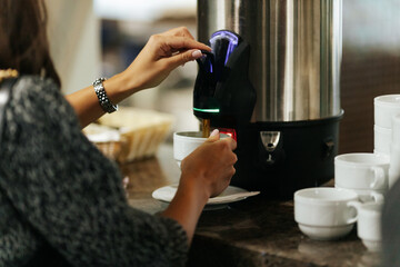 Woman pouring coffee from a thermal dispenser into a cup