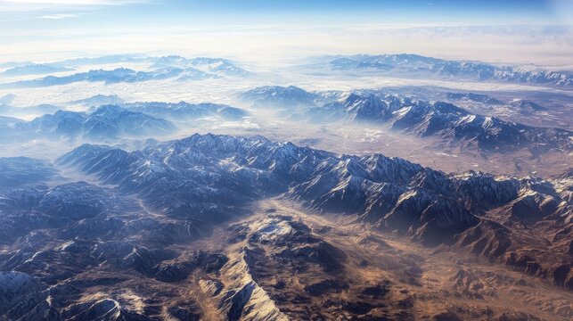 Aerial view of majestic snow-capped mountains under a clear blue sky, showcasing rugged terrain and expansive valleys, capturing the beauty of nature's landscape