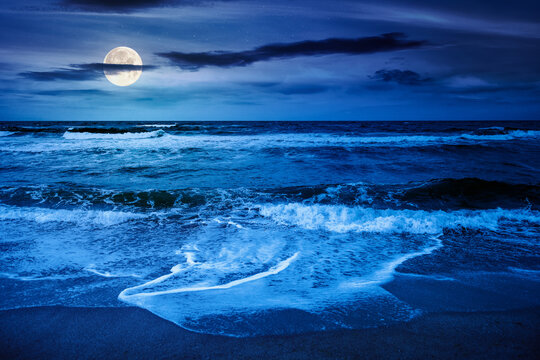 black sea waves crashing sandy beach at night. summer vacation on a windy weather under dark cloudy sky in full moon light. view of dramatic seascape. background for investment or abstract concepts