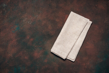 Linen beige napkin on dark grunge background, flat lay, top view, copy space