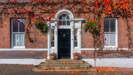 Traditional brick house entrance with black door and autumn ivy