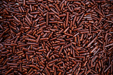 Full frame overhead background of brown, stick-shaped chocolate sprinkles