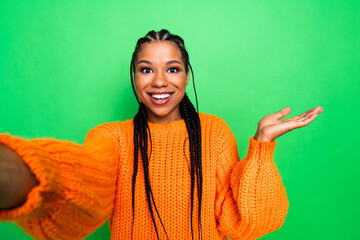 Young woman takes a cheerful selfie in a bright orange knit sweater against a green background...
