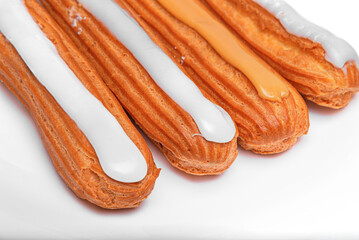 Four elongated choux pastries, eclairs, topped with white and caramel-colored icing on a bright white surface.