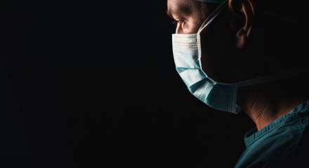 A determined medical professional is immersed in deep concentration, wearing a protective face mask against a stark backdrop, conveying a sense of focus and commitment.