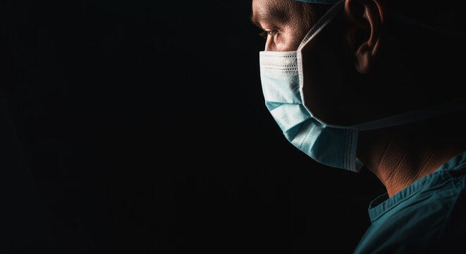 A determined medical professional is immersed in deep concentration, wearing a protective face mask against a stark backdrop, conveying a sense of focus and commitment. - Powered by Adobe