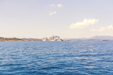Cruise ships docked in Corfu harbor with blue sea and distant hills under sunny sky