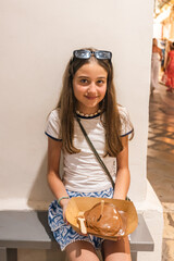 A smiling young girl enjoys chocolate gelato while sitting on a bench in the sunlit alleyways.