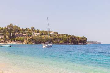 Scenic beach with turquoise sea, pebbles, and a yacht near a Greece village.