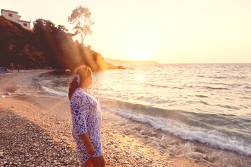 Woman watching sunset on pebble beach during golden hour vacation