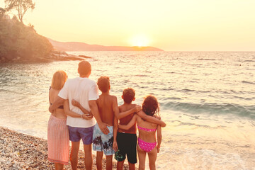 Family of five watching sunset on pebble beach during summer vacation