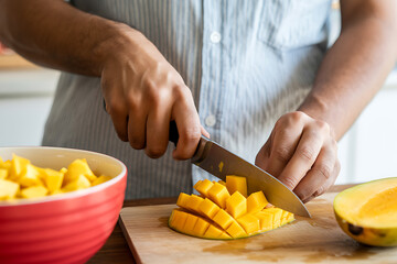 Person slicing ripe mango on a wooden board, preparing fruit for consumption
