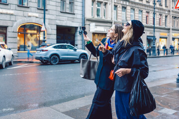 Fototapeta premium Two female friends are walking through city streets and looking at shop windows