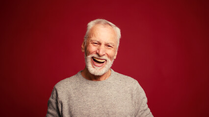 Obraz premium Portrait of smiling happy elderly man laughing looking at camera isolated on red background