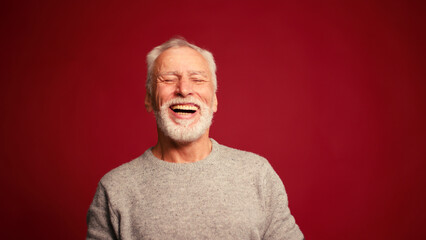 Obraz premium Portrait of smiling happy elderly man laughing looking at camera isolated on red background