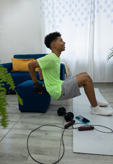 Young man doing tricep dips in his living room, with his hands on a pouf and his feet on a mat. Home workout routine focused on strength and well being