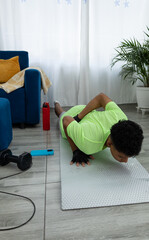 Brown skinned teenager doing a one hand push up in his living room, supported on an exercise mat. Strength exercise and home workout focused on control and endurance
