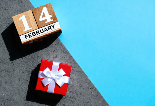 Valentines day calendar with 14 february date wooden blocks, small red gift box with white ribbon on two tone background - Powered by Adobe