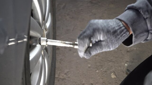 A person wearing gloves is loosening a lug nut on a car tire in a garage. The surroundings are well-lit, and the individual is focused on the task of replacing a wheel.